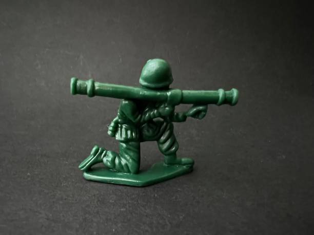 Soldier puppet holding gun towards enemy (black background), war concept.