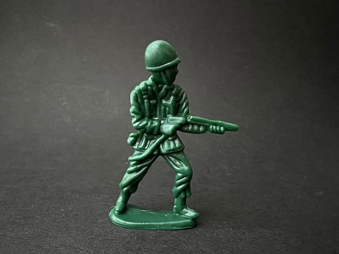 Soldier puppet holding gun towards enemy (black background), war concept.