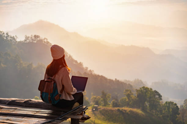 Young woman freelancer traveler working online using laptop and enjoying the beautiful nature landscape with mountain view at sunrise stock photo