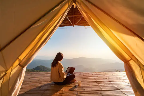 Photo of Young woman freelancer traveler working online using laptop and enjoying the beautiful nature landscape with mountain view at sunrise