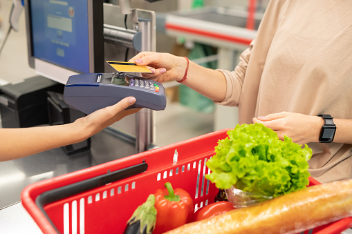 Unrecognizable young woman paying for foods in modern supermarket with credit card