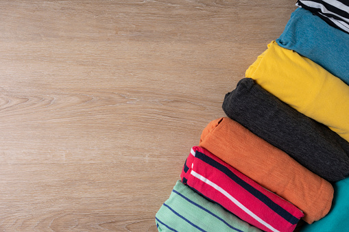 close up of rolled colorful t shirt clothes on wooden table background, travel concept