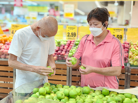 An Asian senior man is spending time with Asian woman shopping for fruits in supermarket.