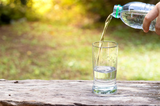 istock Hand holding drinking water bottle pouring water into glass 1401111794
