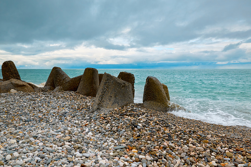 Reinforced concrete breakwaters to strengthen the coast against the backdrop of the sea. Old tetrapods near the white rocks of the village of Gagra. Smooth white pebbles on the seashore.