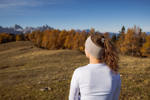 Waist up, view from the back of female hiker with her hair up in a ponytail looking at the view of the mountains while hiking on a beautiful autumn day.