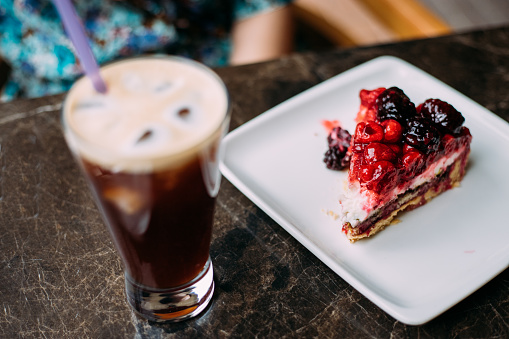 Woman drinking ice americano and eating raspberry, strawberry cake at cafe