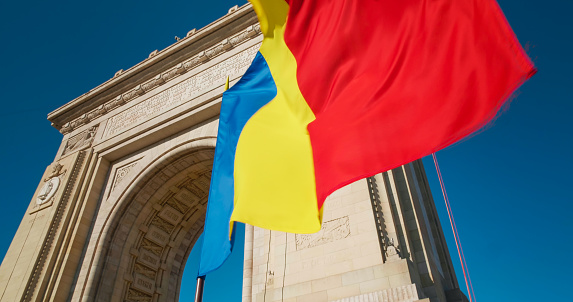 Arc de Triomphe Bucharest. Architectural monument National flag of Romania winding in front of the Arch of Triumph landmark from Bucharest. Romania National Day.