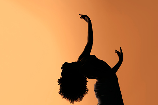 Stock photo of unrecognized confident afro woman dancing against brown background in studio.