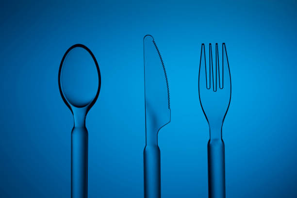 Set of plastic transparent spoon, knife and fork on a blue background. Studio shot.