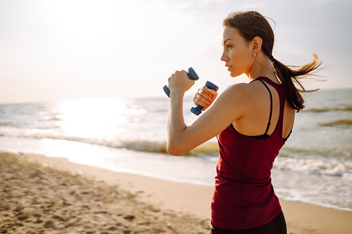 Young woman in sportswear fitness exercise on the beach. Warming up your muscles before an intense workout in the morning. Sport, Active life, sports training, healthy lifestyle.