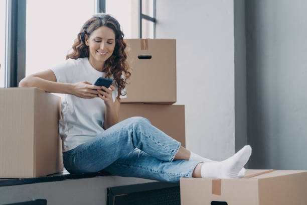 istock Happy spanish woman is sitting on windowsill texting on phone and unpacking boxes. 1401129323
