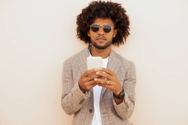 Focused African American man video calling outdoors. Man in suit with beard holding mobile phone. Communication, technology concept