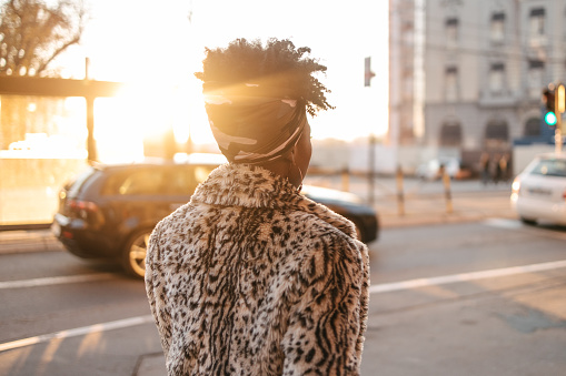 A rear view of an African woman walking down the city street in an animal print coat.