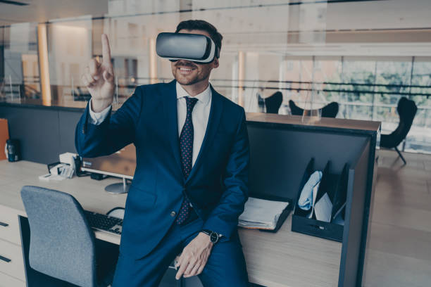 istock Businessman sitting on desk in office and using VR headset on his head, pointing with forefinger 1401136334