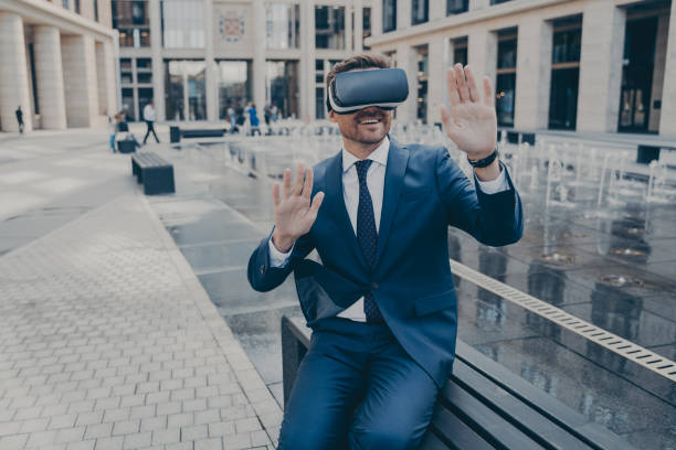Handsome businessman sitting outside on bench while wearing portable Virtual Reality glasses
