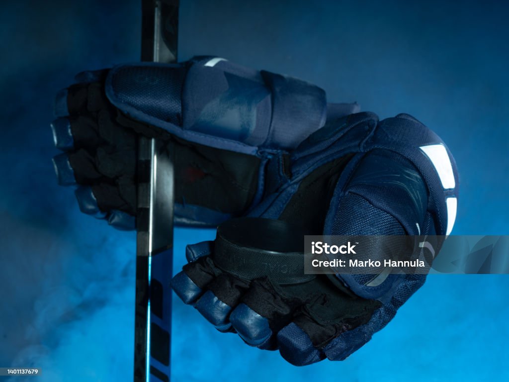 Closeup of ice hockey equipment against a smoky background. Hockey puck, ice hockey stick, ice hockey gloves Helsinki / Finland - JUNE 2, 2022: Closeup of ice hockey equipment against a smoky background. Hockey puck, ice hockey stick, ice hockey gloves Blue Stock Photo
