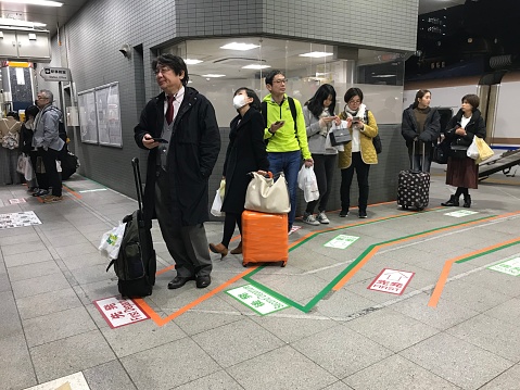 Tokyo, Japan - 22 December 2018: A group of passengers are queuing on the Shinkansen platform in Tokyo Station. These people are from a variety of backgrounds from businessman to housewives. It is easy for travelers to board their train in Japan, since there are many signs and lanes with clear directions even without any comprehension of Japanese language.