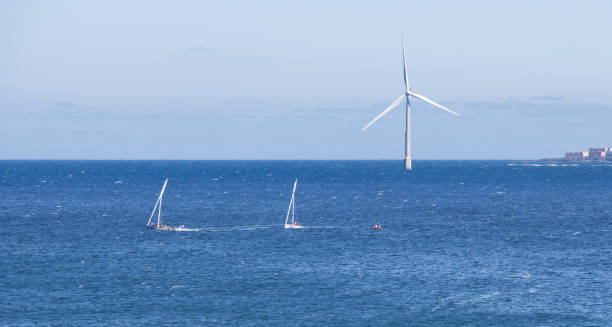 Two small lateen sailboats sail near an offshore wind turbine on the island of Gran Canaria stock photo