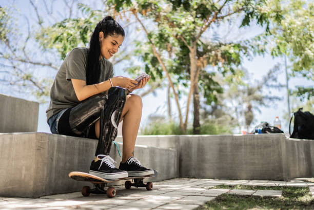 une skateuse handicapée utilisant un téléphone portable au parc - prosthetic equipment photos et images de collection