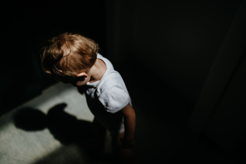 A dark high angle view portrait of sad anonymous little baby girl looking down.