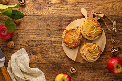 Mini Apple pie tartlets with walnut on wooden table. Delicious dessert for autumn winter dinner.Top view.