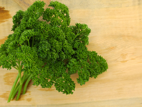 Bunch of curly parsley on a wooden background. Fresh green parsley top view. Sprigs of curly parsley close-up.