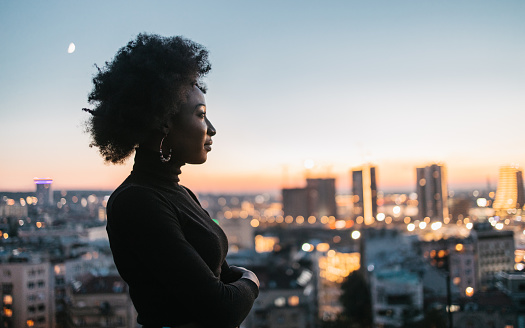 A rear view of a young African woman on a rooftop looking at the city landscape.