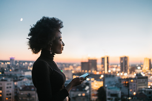 A rear view of an young African woman on a roof top looking a the city landscape.