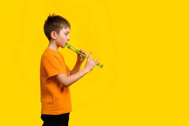 Concentrated Child Boy 9-11 y.o in Basic Orange T-shirt Plays Block Flute on Yellow Background. Concept of Music Education and Training in Music School on Wind Instruments