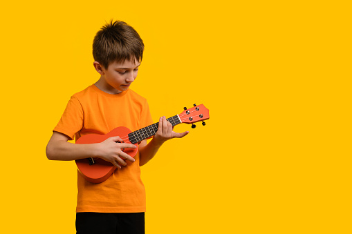 Child play acoustic Ukulele guitar on yellow background. Hawaiian small guitar. Concept of Music Education and Training Practice in Music School