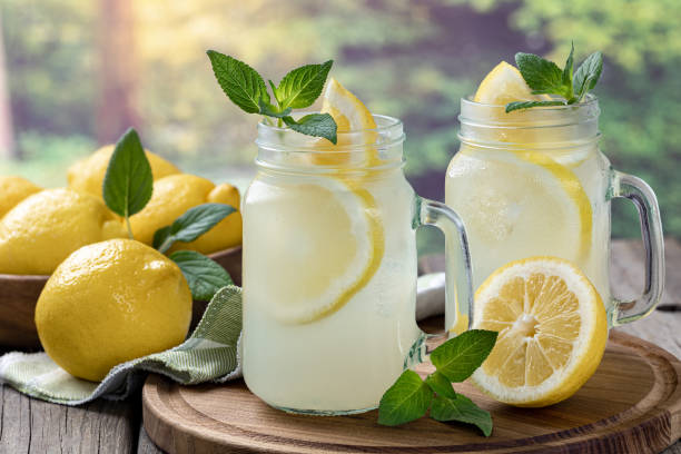 Two glasses of lemonade with mint and lemons Two glasses of lemonade with mint and lemon on a wooden tray with rural background lemonade stock pictures, royalty-free photos & images
