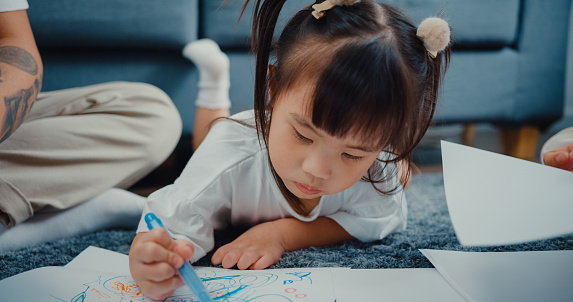 Close up young parent Asian family sitting on floor  enjoy with golden time happy moment together with their child playing art drawing painting paper in living room at home. Family happy moment concept.
