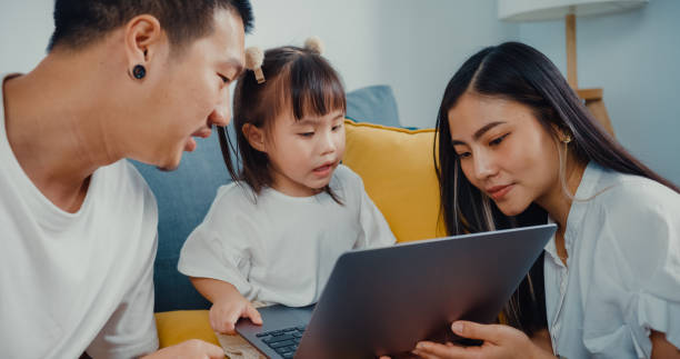 young parent asian family sitting on couch  enjoy with golden time happy moment together with their child use laptop watch cartoon movie in living room at home. - father digital tablet asian ethnicity daughter imagens e fotografias de stock