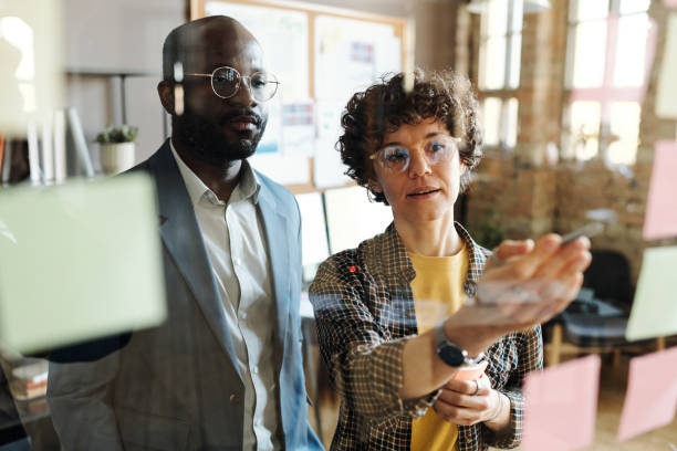 istock Colleagues reading sticky notes on glass wall office 1401153978