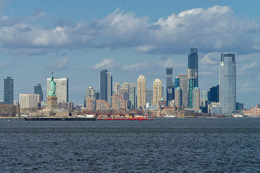 Panoramic view of the New Jersey coast and urban skyline from a ferry boat on the Hudson River, New York, USA. In the foreground is the Statue of Liberty.