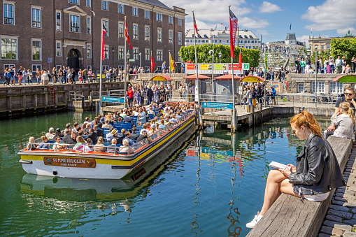 Young girl sitting reading on a harbor pier at Nyhavn which is a very popular tourist spot in the center of Copenhagen