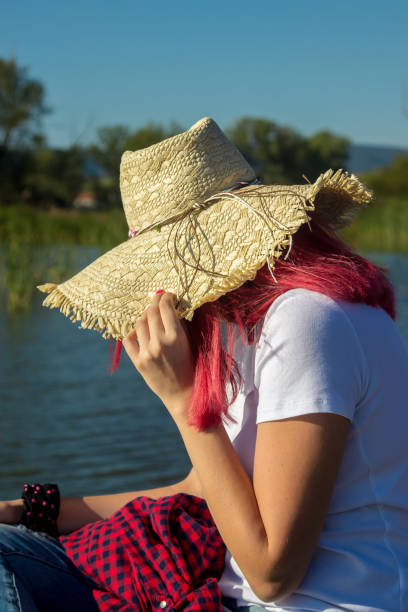 Woman is wearing straw hat looking on the beautiful lake
