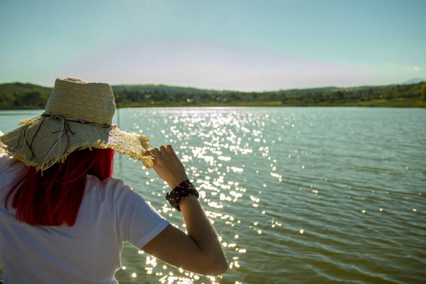 Woman is wearing straw hat looking on the beautiful lake