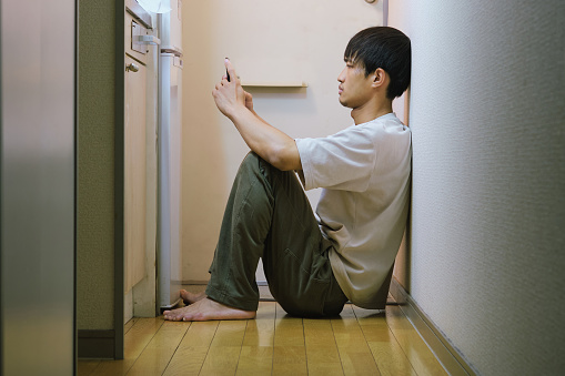 man looking at smartphone while sitting on wooden floor in small apartment in japan