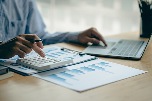 En el mostrador de contabilidad, un contador presiona una calculadora para analizar los gráficos de inversión para generar informes financieros mensuales o ganancias de la empresa. photo