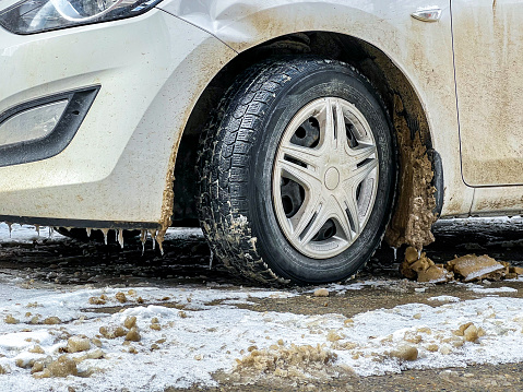 A medium shot of a senior, Caucasian man fixing snow chains onto his car tyres.