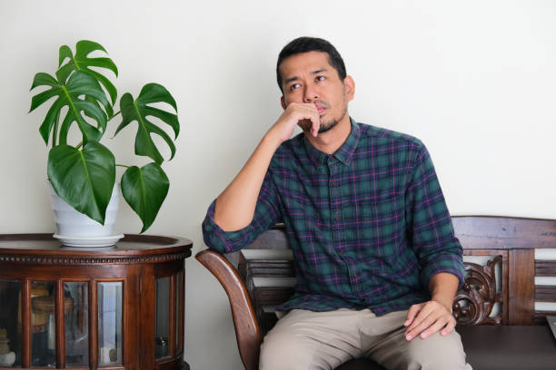 Adult Asian man thinking about something with sad expression when sitting alone in a couch