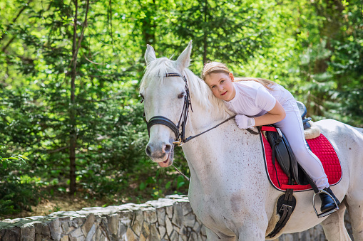 A teenage girl with her favorite white horse for a walk in the spring forest. Communication with animals in nature. Horizontal photographs of animals and people.