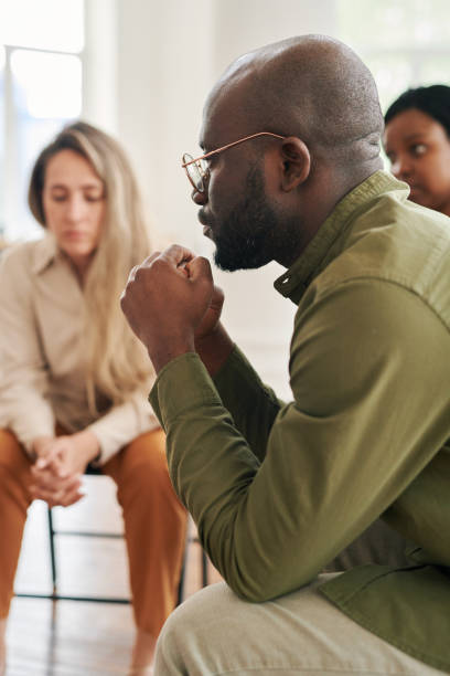 istock Side view of young stressed man with interlocked hands by face attending session 1401166622