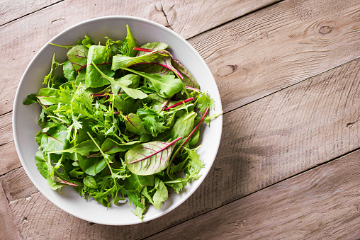 Green Salad Mix. Healthy green salad, fresh organic leaves mix salad with arugula, swiss chard and lettuce, wooden background, top view, copy space.