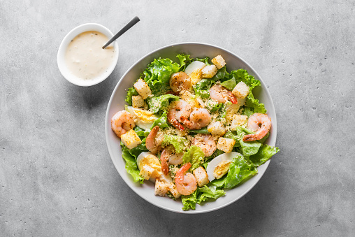 Shrimp Salad. Seafood Caesar Salad with prawns, parmesan cheese and caesar dressing on gray stone background, top view, copy space.