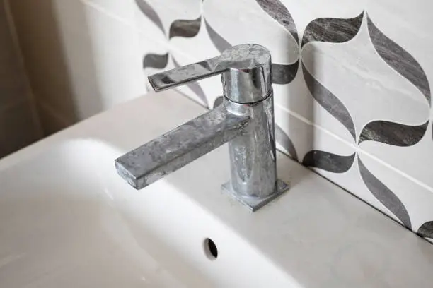 Dirty faucet with limescale, calcified water tap with lime scale on washbowl in bathroom