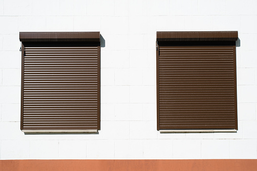 Two windows closed with roller shutters exterior view of white wall of building, outdoors.