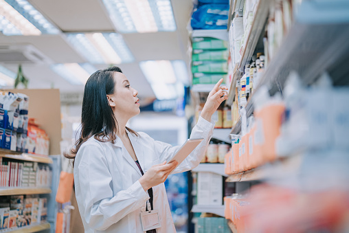 Asian Chinese female Pharmacist checking inventory at shelf in retail pharmacy